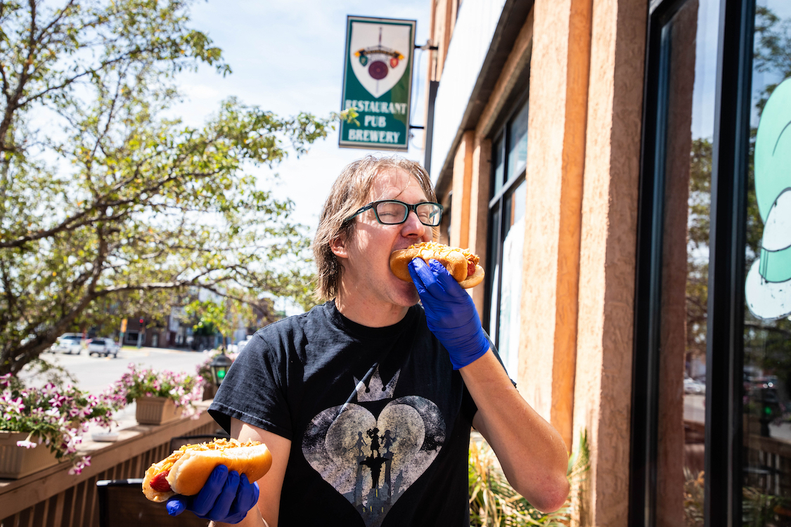 This photo shows Sean Dempsey, wearing a black T-shirt, biting into a hot dog and holding another one in the other hand.