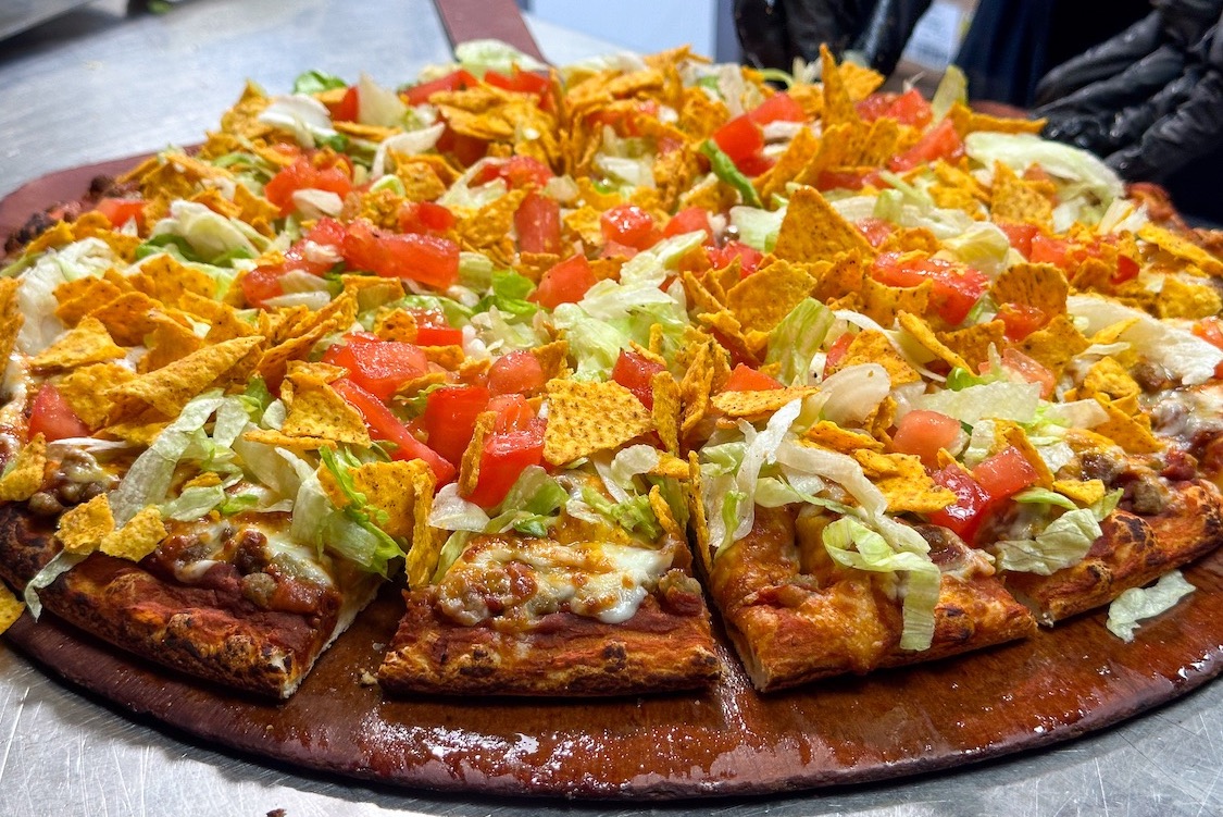 This photo shows a taco-themed pizza from Happy Joe's, with ground beef, corn chips, sliced tomatoes and lettuce.