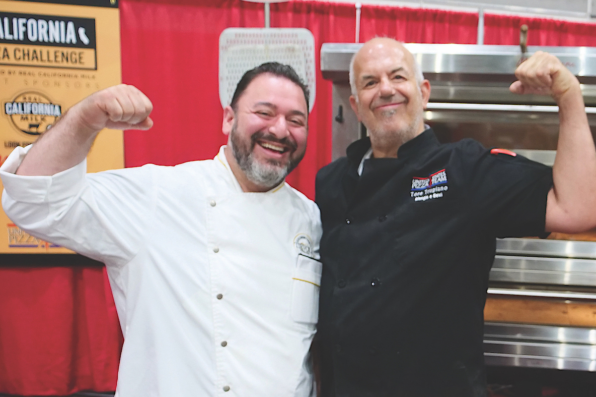 This photo shows two male USPT members, one in a white chef coat and the other in a black coat, flexing their muscles and smiling proudly.