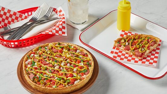 This photo shows a deep-dish pizza topped with hot-dog meat, onions, sliced jalapeños and other ingredients.