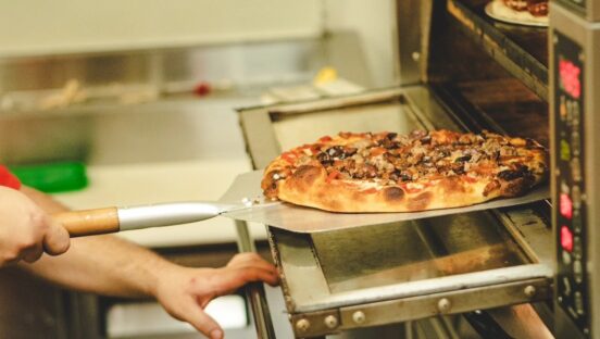 This photo shows someone peeling a pizza out of a deck oven.