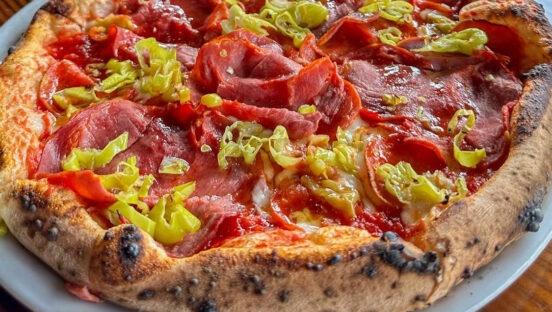 This photo features a pizza topped with mozzarella, capicola, pepperoni and pepperoncinis.