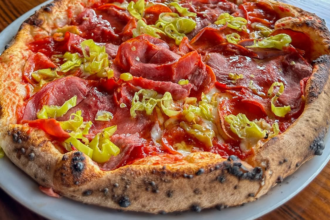 This photo features a pizza topped with mozzarella, capicola, pepperoni and pepperoncinis.