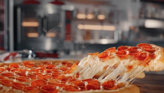This photo shows a slice of pepperoni pizza being pulled from a whole pie, with a great cheese pull.