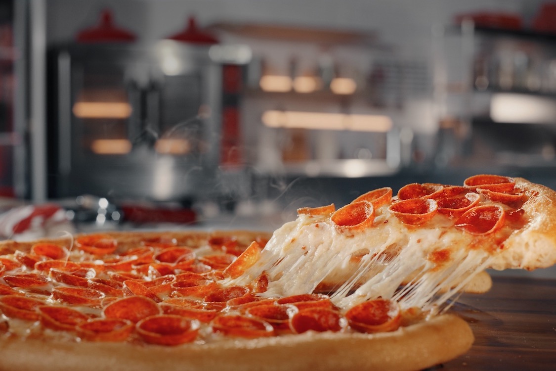 This photo shows a slice of pepperoni pizza being pulled from a whole pie, with a great cheese pull.