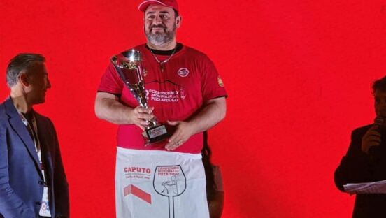 This photo shows Giovanni Labbate holding his Caputo Cup trophy and standing in front of a red backdrop.