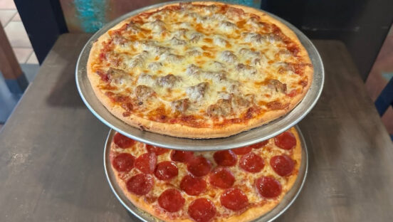 This photo shows a stack of two pizzas on trays.