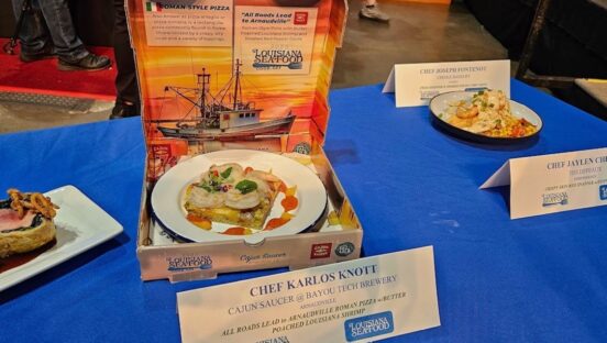 This photo shows the contest-winning pizza, a small Roman-style pie topped with whole shrimps, in a pizza box on the table with other entries.