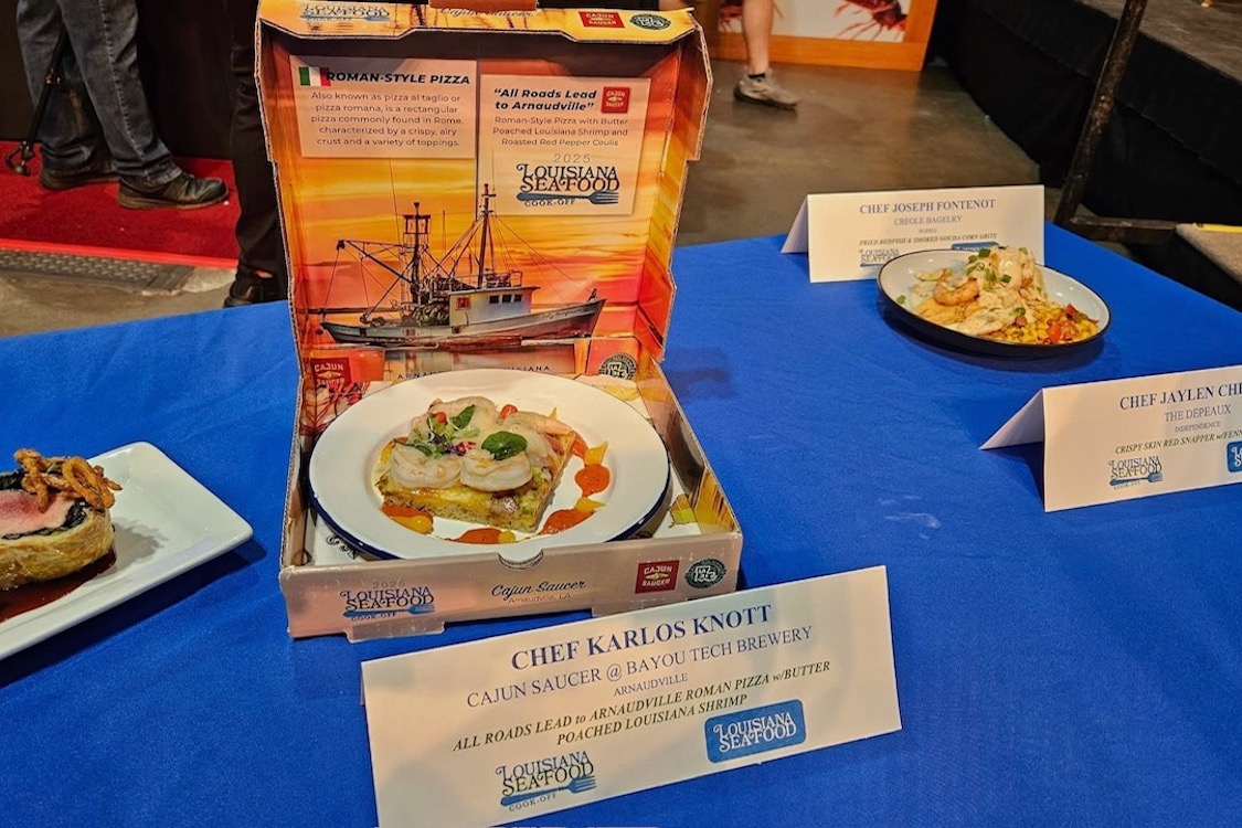 This photo shows the contest-winning pizza, a small Roman-style pie topped with whole shrimps, in a pizza box on the table with other entries.