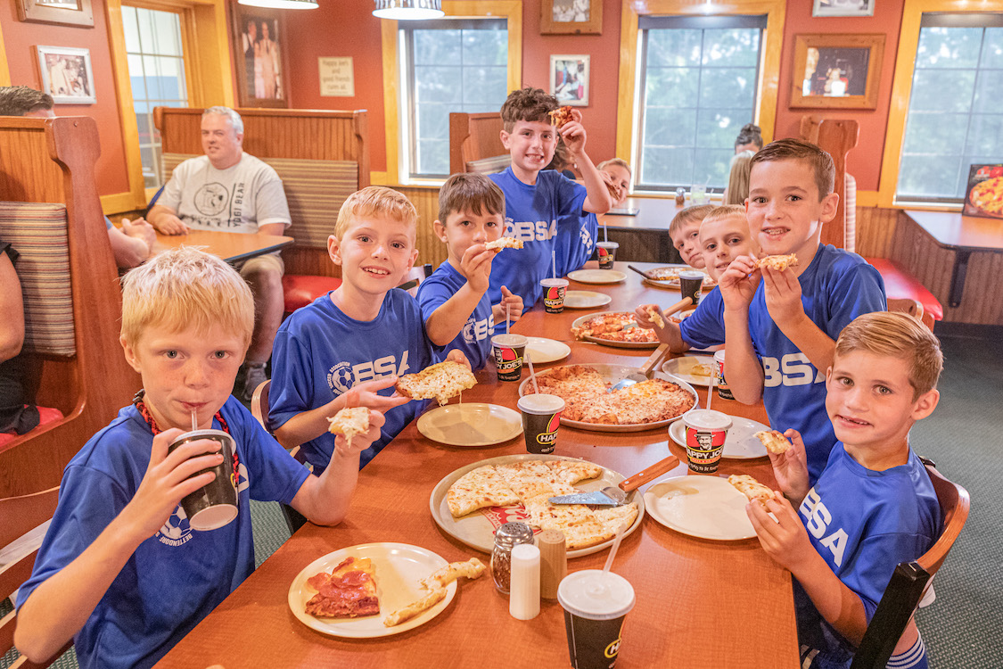 This photo shows a team of soccer-playing boys looking at the camera while enjoying a pizza party at Happy Joe's.