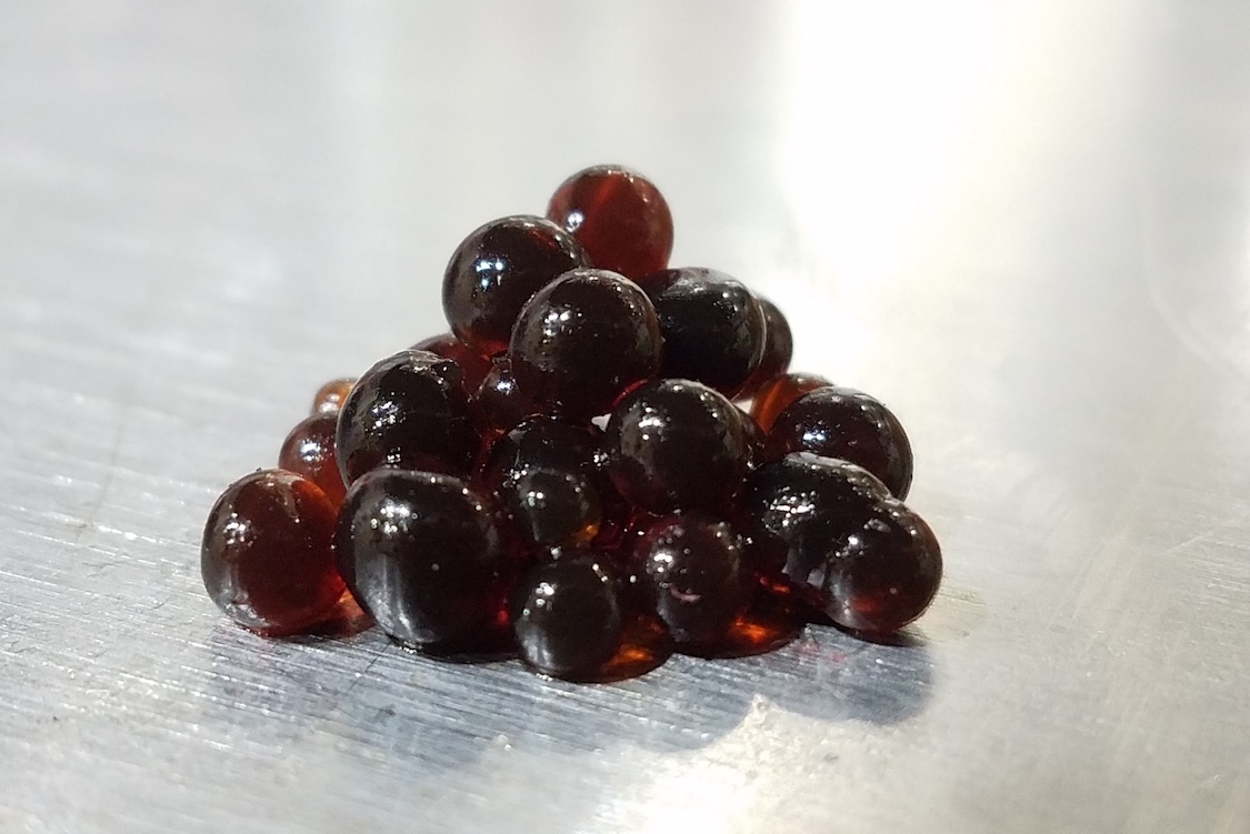 This photo shows a pyramid of beautiful dark Balsamic pearls against a white backdrop.