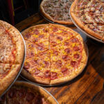 This photo shows an array of pizzas from Mikey's Late Night Slice, with a large pepperoni pie in the center.