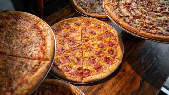 This photo shows an array of pizzas from Mikey's Late Night Slice, with a large pepperoni pie in the center.