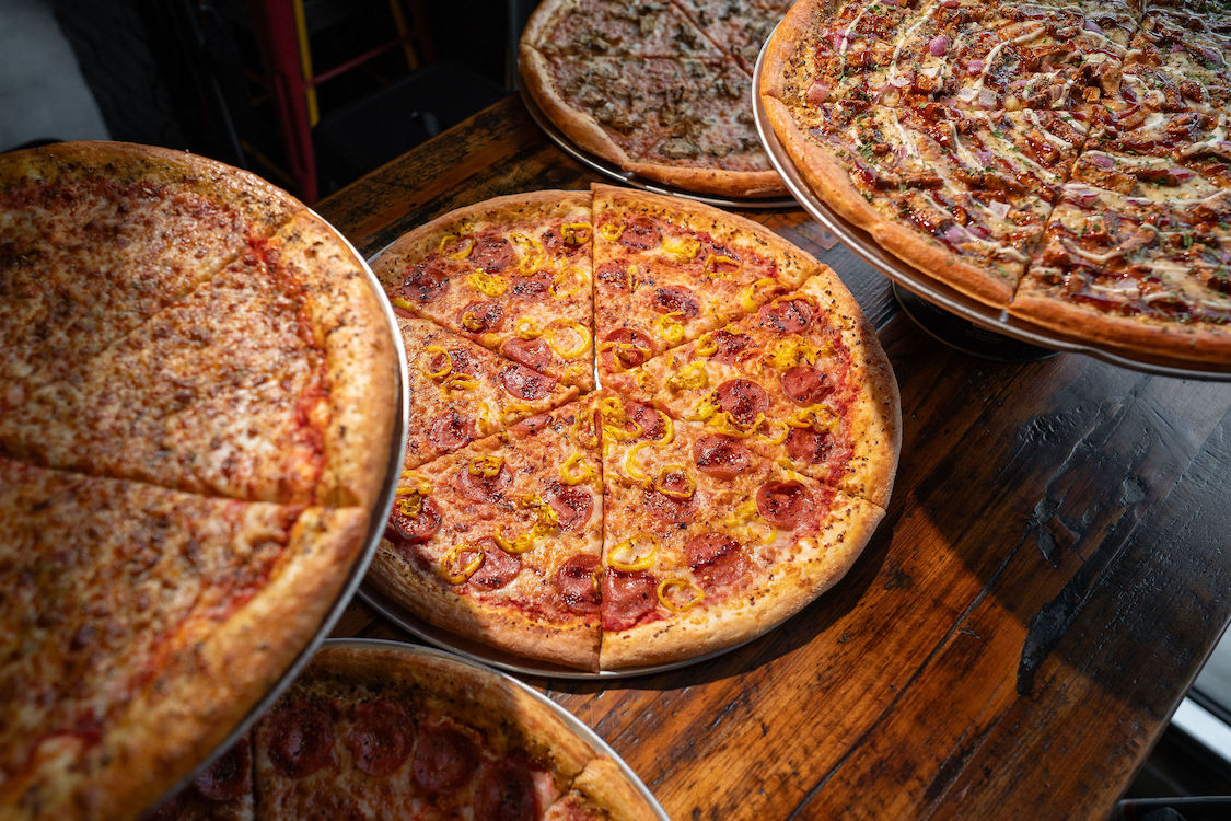 This photo shows an array of pizzas from Mikey's Late Night Slice, with a large pepperoni pie in the center.