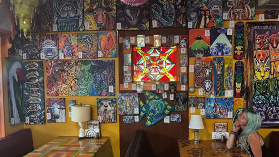 This photo shows a female customer sitting at a table and peering up at the elaborate artwork decorating one wall at Satchel's Pizza.