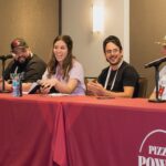 This photo shows four panelists in a dough-making session at the 2024 Pizza Power Forum. They're sitting at a table covered with a red cloth that has the Pizza Power Forum logo on it.