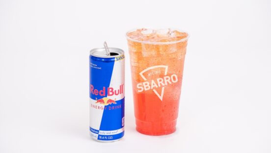 This photo shows a can of Red Bull next to a plastic cup filled with ice and lemonade.
