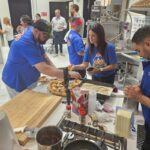 This photo shows several USPT chefs gathered around a prep table as they work on making their pizzas in the Galbani kitchen.