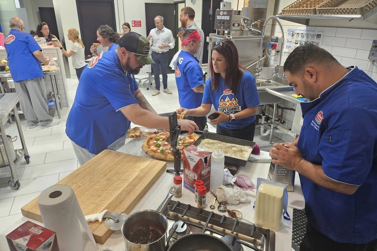 This photo shows several USPT chefs gathered around a prep table as they work on making their pizzas in the Galbani kitchen.