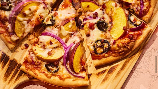 This photo shows a pizza topped with peach slices, mozzarella, bacon, red onion slices and jalapeños.