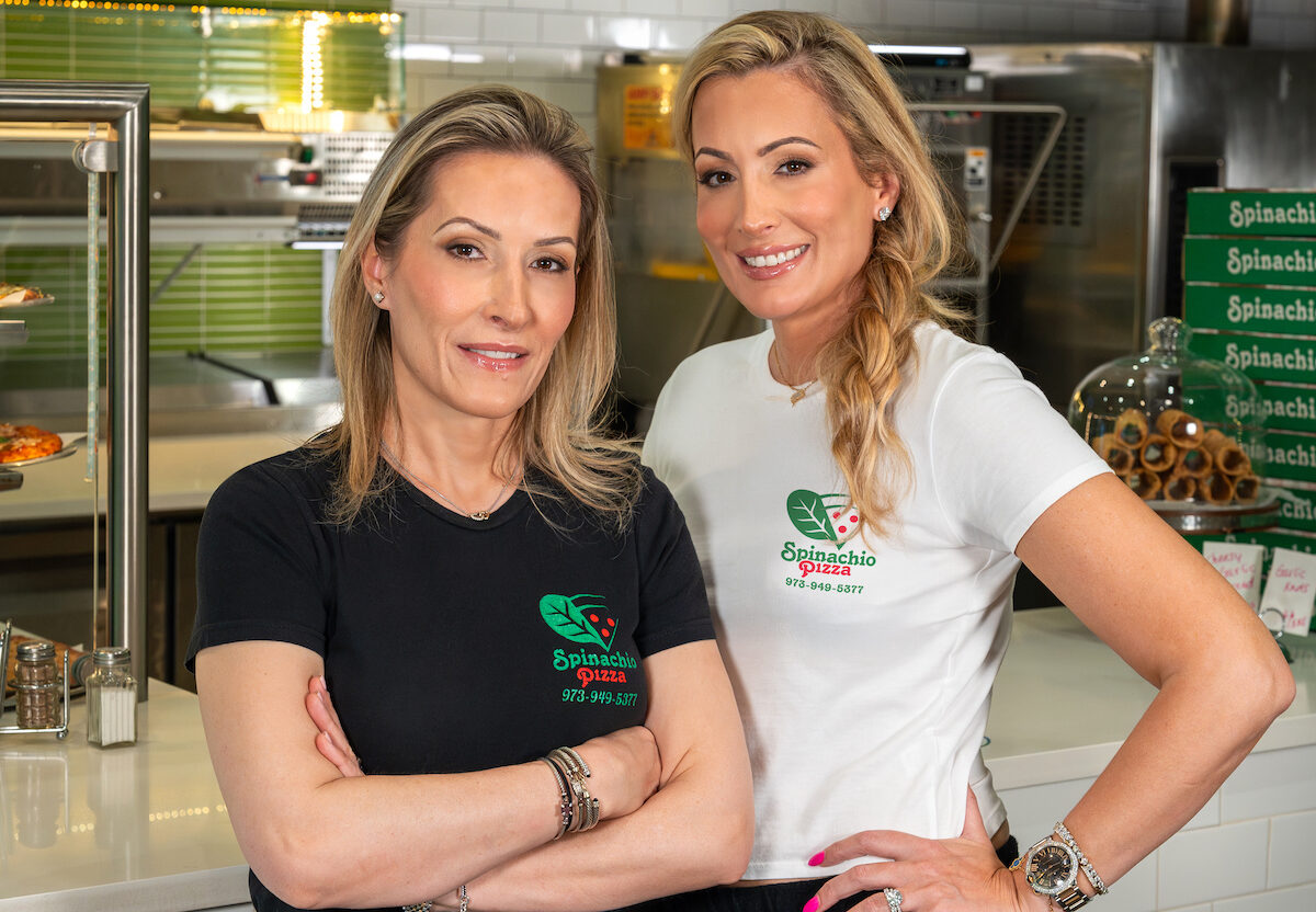 This photo shows the two women who own Spinachio Pizza standing close together, one wearing a black t-shirt and the other in white.