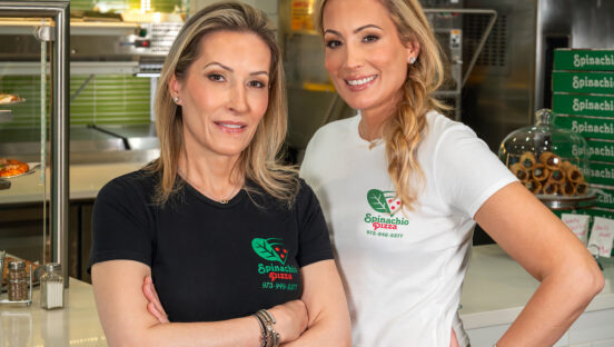 This photo shows the two women who own Spinachio Pizza standing close together, one wearing a black t-shirt and the other in white.