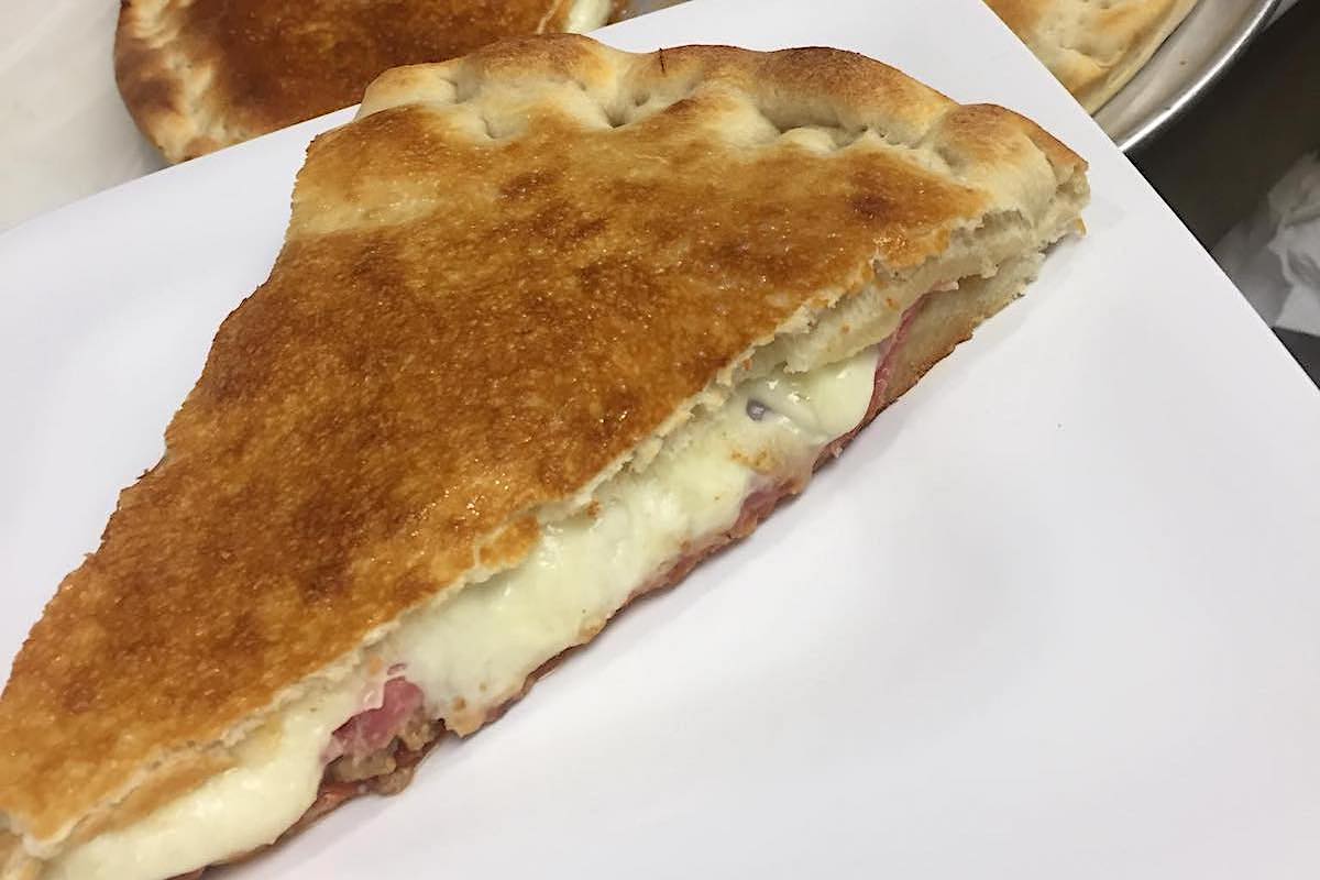 This photo shows a pizza stuffed with six meats and three layers of cheese on a paper plate.