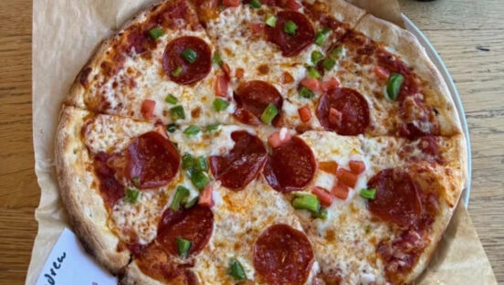 This photo shows a pizza topped with pepperoni and chopped bell peppers.
