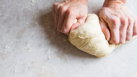 This photo shows a man's hands kneading pizza dough on a white table.