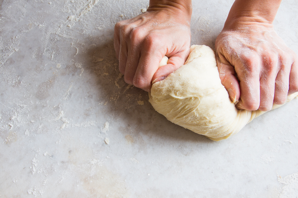 This photo shows a man's hands kneading pizza dough on a white table.