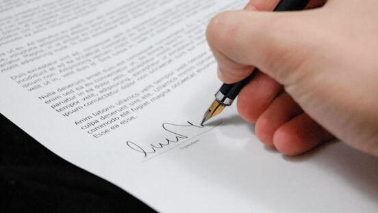 This photo shows a man's hand signing a lease with a pen.