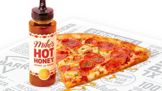 This photo shows a slice of New York-style pepperoni pizza with a bottle of Mike's Hot Honey sitting next to it.