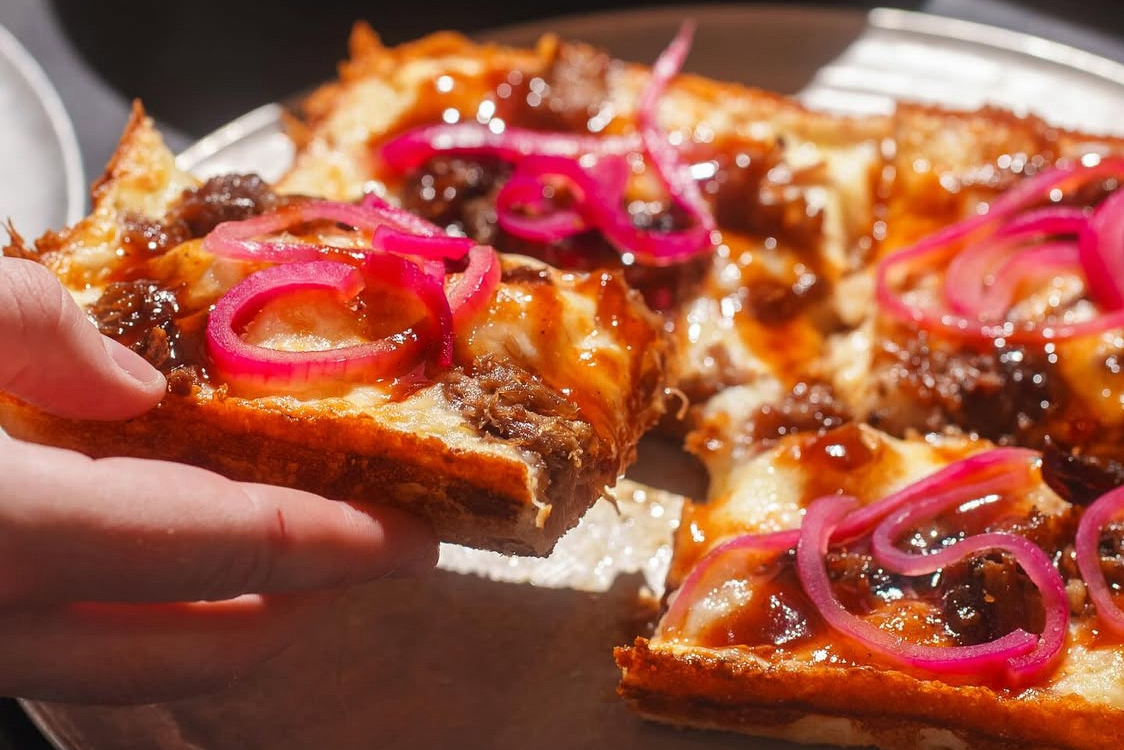 This photo shows a square Detroit-style pizza topped with red bell peppers and BBQ pulled pork.