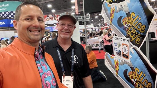 This photo shows Matt Plapp, wearing an orange jacket, shooting a selfie with Andy Dell at the Pizza Expo.
