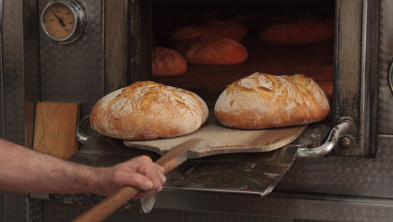 This photo shows two beautiful loaves of bread being peeled out of a restaurant's oven.
