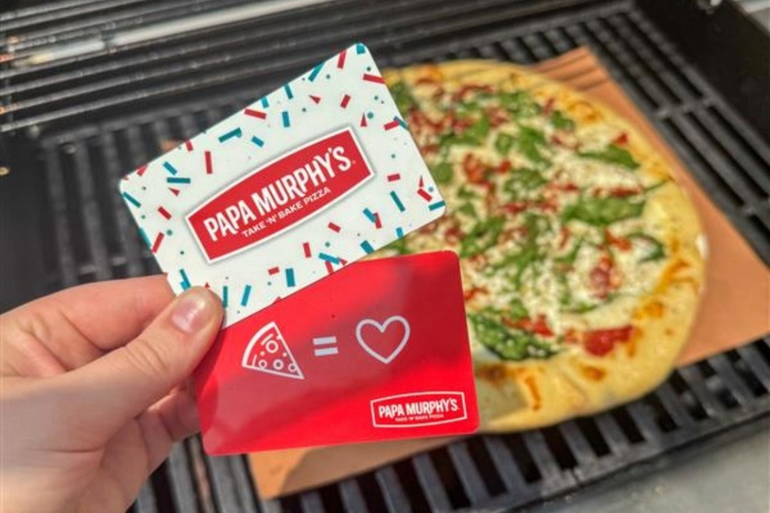 This photo shows a Papa Murphy's gift card held in someone's hand with a baked pizza coming out of a home oven in the background.