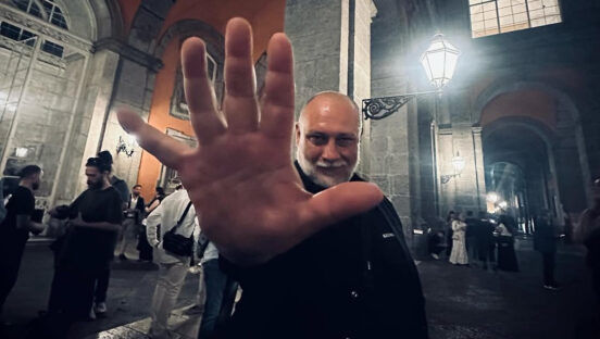 In this dramatic photo, Francesco Martucci, dressed in black, holds his open hand in front of the camera while standing in a very large room somewhere in Italy.