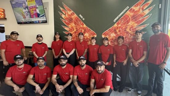 The photo shows a group of Mountain Mike's employees standing or kneeling in the restaurant, all wearing red shirts and black pants.