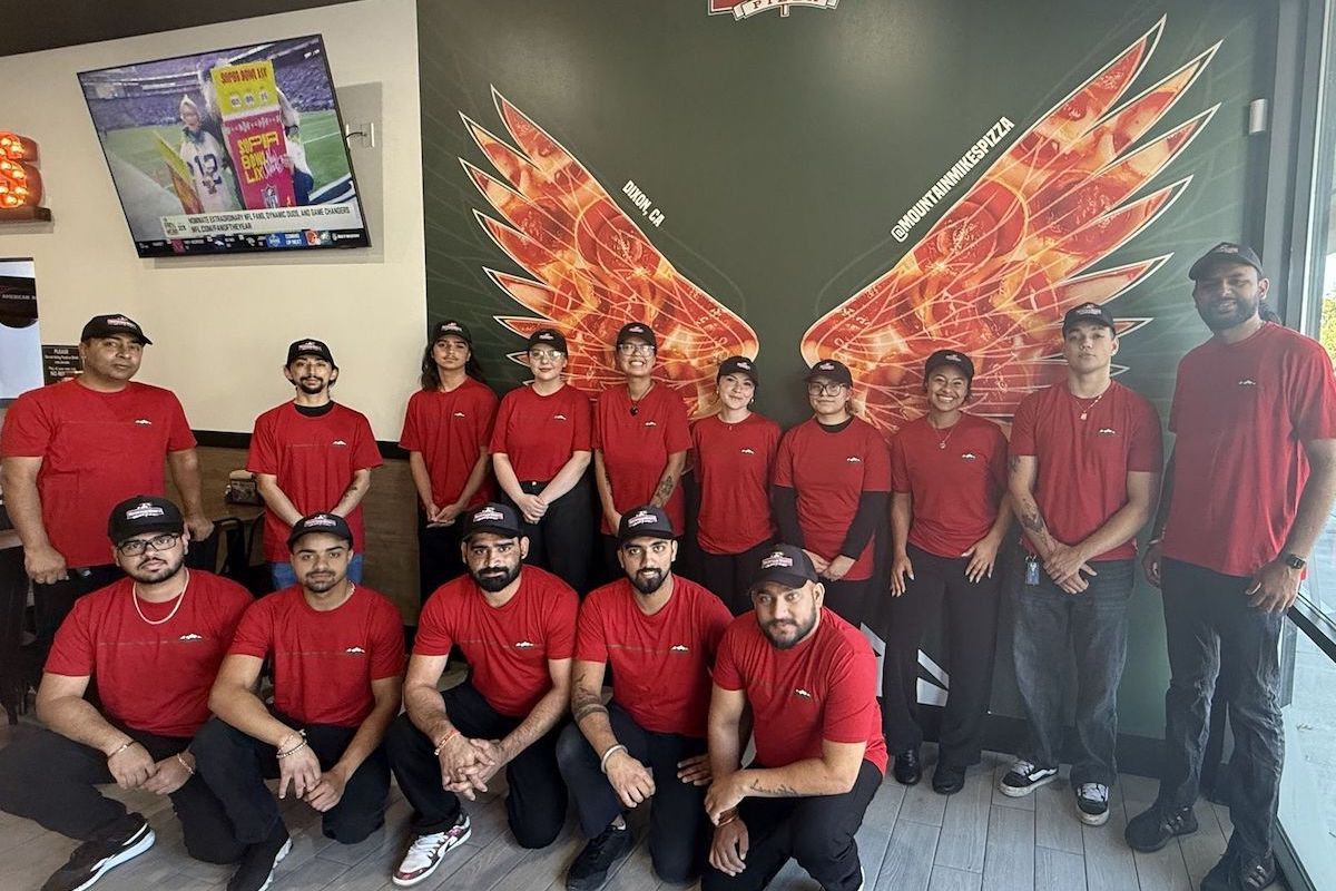 The photo shows a group of Mountain Mike's employees standing or kneeling in the restaurant, all wearing red shirts and black pants.