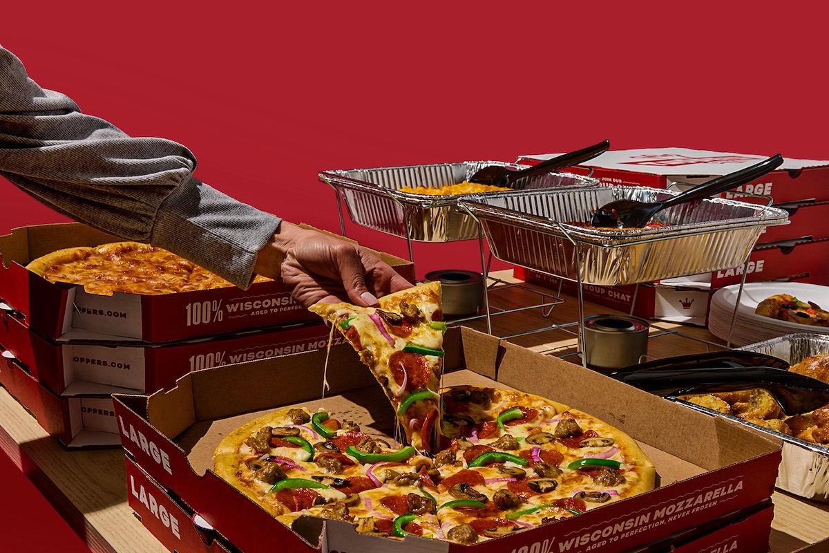 This photo shows a man's arm and hand as he pulls a slice of pizza from a whole pie.
