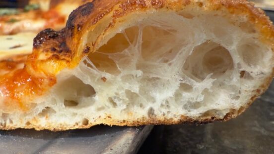 This photo shows an up-close view of a pizza crust's open crumb structure with large pockets.