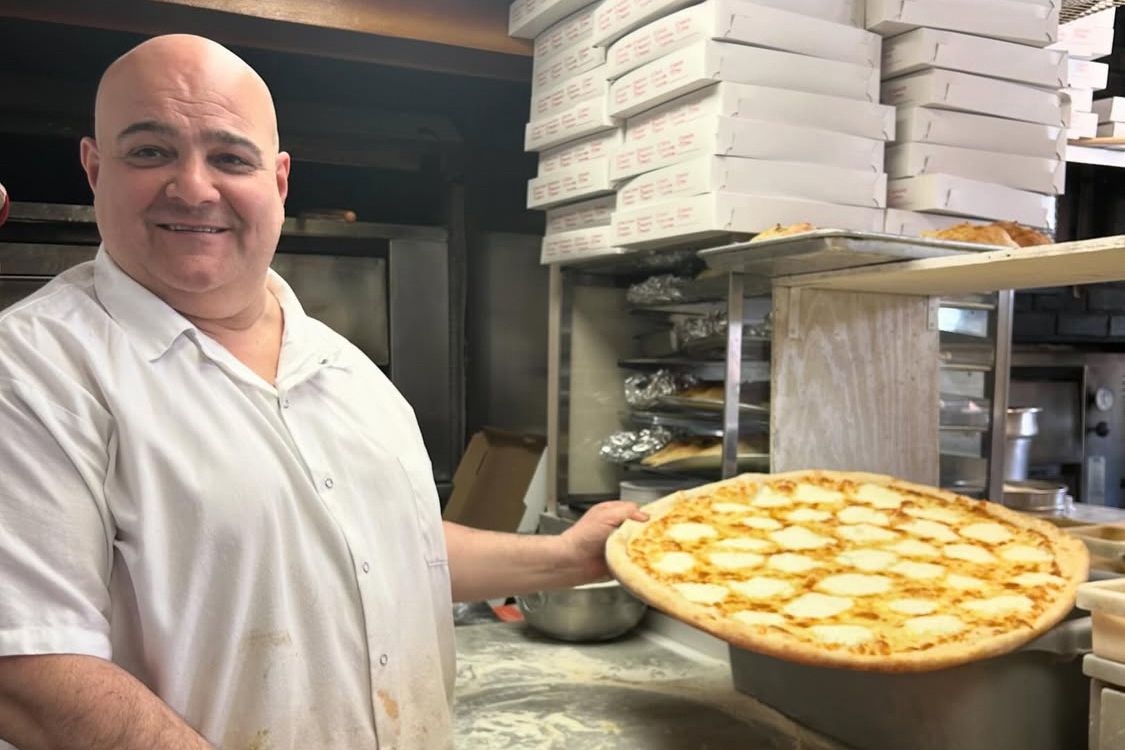 This photo shows Cosimo Tiso, wearing a white shirt, holding one of his white pies in the kitchen at Louie & Ernie's Pizza.