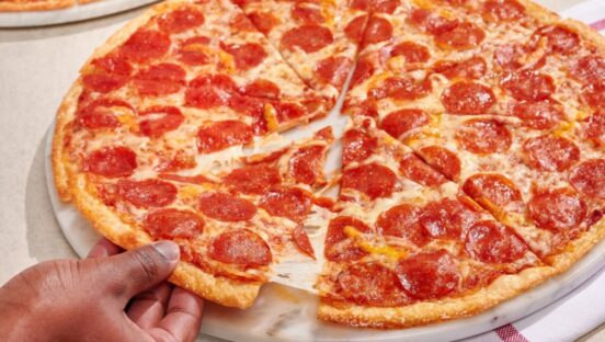 This photo shows a man's hands pulling a slice from a whole pepperoni pizza.