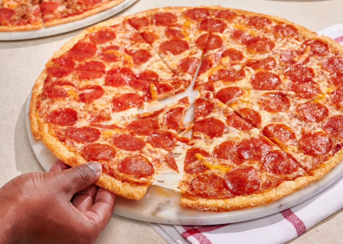 This photo shows a man's hands pulling a slice from a whole pepperoni pizza.