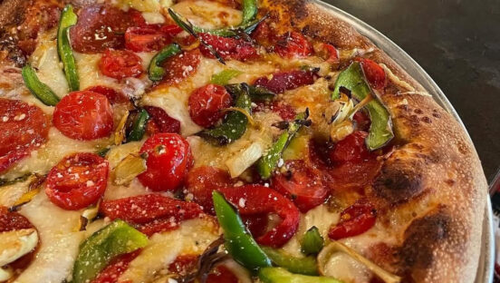 This photo shows a round pizza topped with cherry tomatoes, bell peppers and onions.
