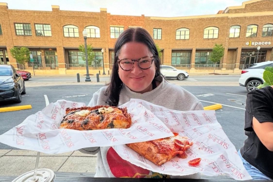 This photo shows a female customer holding paper plates with two slices of pizza from Slice House.