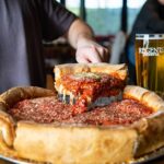 This photo shows someone removing a slice of deep-dish pizza from a whole pie.