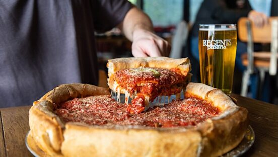 This photo shows someone removing a slice of deep-dish pizza from a whole pie.