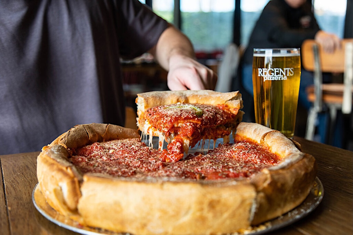 This photo shows someone removing a slice of deep-dish pizza from a whole pie.