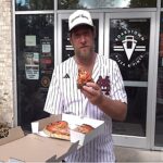 This photo shows Dave Portnoy holding a slice of pizza and standing in front of Boardtown Pizza & Pints in Starkville.